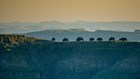 View of seven bison on on a ridge with ridges stretching into the distance behind. 