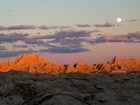 The setting sun illuminates several sharp ridge lines under a moon. 