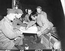 A man points to locations on a map. Other men look on.