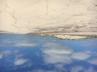 Large sand dunes tower over a flat, sandy beach under a blue sky with gray clouds.