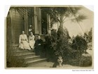 Family poses on steps of Victorian home. 3 Women, seated, bearded man stands. Dog in foreground