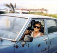 Women with sun glasses smiles from inside her beat up blue car.