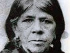 Indigenous woman with dark braids looks directly into camera