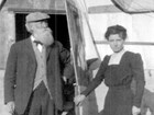Photo of woman in simple dress standing next to old man with beard in front of tent home.