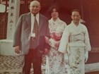 Two Japanese women in kimonos stand next to man in suit and tie, posing before temple