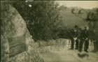 two men sit on rock wall, behind them is large area of trees and shrubs