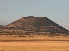 photo of a dry grassy field with a cinder cone in the distance