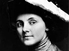Young woman in large hat and high-necked shirt with large button smiles at camera