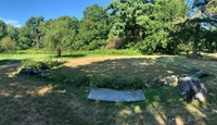 A low stone wall marks 3 sides of a house foundation in an open field.