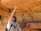 photo of a person pointing at trace fossils in rock above on an over hanging rock