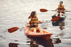Two kids paddling kayaks on a lake.