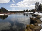 A calmly flowing river winding through an area with conifer trees and snow covered shores.