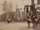 An 1864 stereograph shows men on horseback looking at burned out buildings.