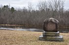 A round boulder atop a stone pedestal rests in a winter landscape.