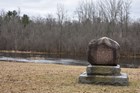 A round boulder atop a stone pedestal rests in a winter landscape.