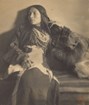 A seated woman wearing beads and with long hair looks to her right