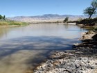A brownish river with rocky banks and the shadows of trees on the water.
