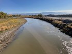 A narrow river along a dirt road and road debris on one side and gravel bank on the other side.