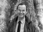 Man wearing glasses and NPS uniform stands in front of the trunk of a sequoia tree.