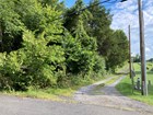 A two-track road extends from a paved roadway bordered by woods and a cemetery.