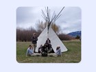 7 young people in AmeriCorps uniforms pose in front of teepee. Mountain behind.