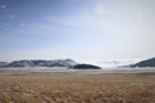 A wave of fog spills over a hill into a grassy valley.