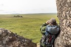 A backpacker looks at granite tors across the tundra through binoculars.