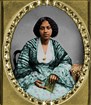 Colorized photo of African American woman in the 1850s wearing a large dress and holding a book.