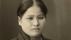 Asian woman in dark kimono, wearing classes, in a formal portrait