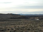 Beyond a large open prairie, are low gray hills with a creek and a distant chain of mountains.
