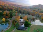 Aerial image of autumn wooded hills and meadows with low buildings, with two ponds.