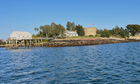 A rocky wooded island sits atop placid dark blue waters. 