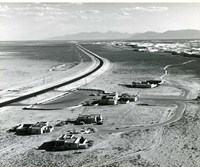 High angle view of a park district shows a parking lot and a cluster of low adobe buildings