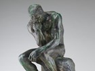 Sculpture of a man seated on a rock with his chin resting on his fist while in contemplation.