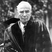 J. Robert Oppenheimer as an old man, wrinkled with white hair, wearing university graduation robes.