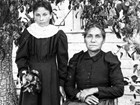 Dated black and white portrait of seated woman and young girl standing in front of house