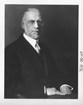 An older man seated for a formal portrait in a suit and tie. The portrait is in black and white.