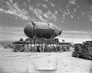 Large bomb on a truck with a line of men standing in front 