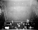 Black and white overhead photo of a large wall of wires and people in lab coats working in clusters