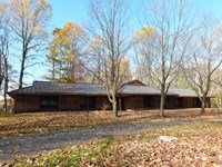 A long, one-story structure is surrounded by turf, autumn trees, and a slightly curving driveway