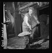 Black and white woman in coveralls and headscarf shoveling woodships into furnace 
