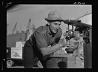 Black and white photo of a white man in a hat adjusting mechanical equipment