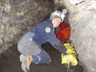 Caver preparing to enter a crawl inside of a cave.