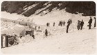 Black and white picture of people watching plows clear snow. 