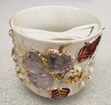 A dainty looking porcelain tea cup with a curved shield-like object attached over the rim.