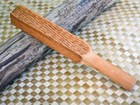 Rectangular wooden tool with diagonal carvings on surface sits on barkcloth with imprint of design.