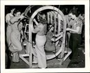 Black and white photo of 4 white women screwing bolts into cylindrical frame 