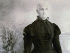 Portrait of an austere woman in high-neck black dress with corset and puffy sleeves.