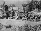 black and white image of Black woman in hat sitting in front of rustic cottage.