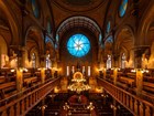 Synagogue interior with side balconies, a chandelier, and a circular stained-glass window.